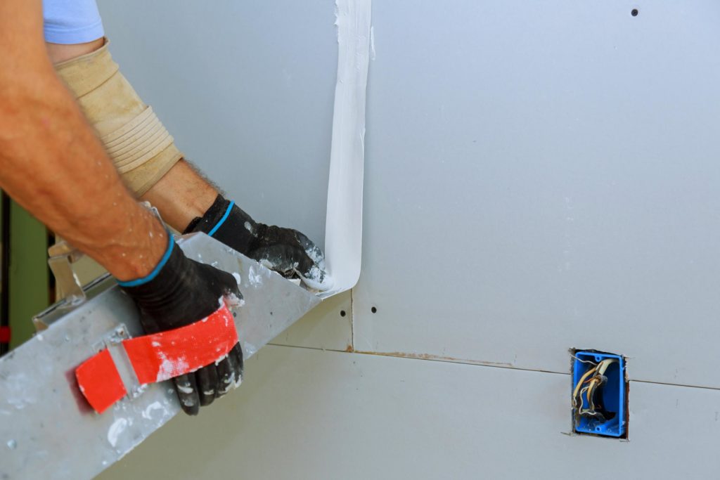 trabajador instalando tablero de yeso en pared interior scaled